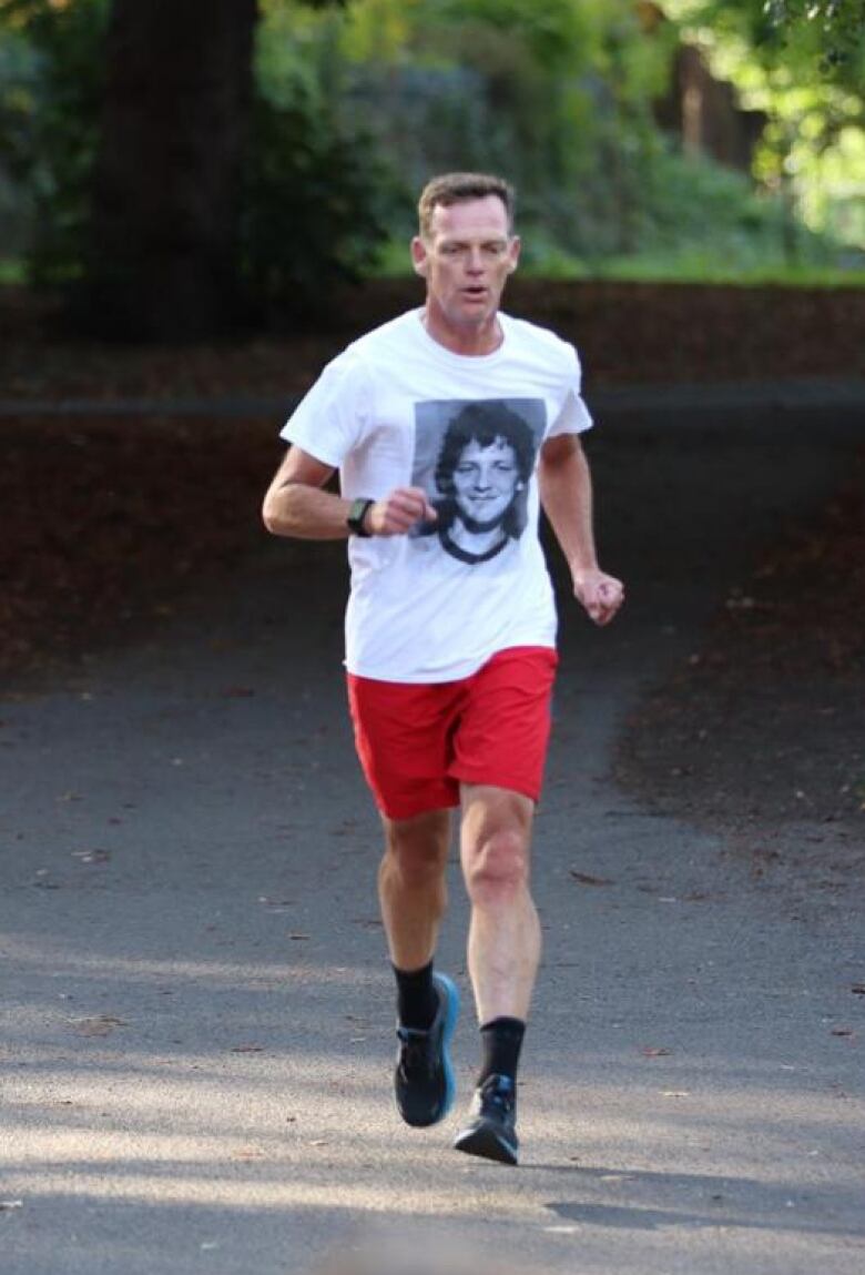 A man running in red shorts and a white T-shirt with a black and white image of a smiling young man's face. 