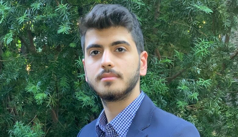 A headshot of a young man in a suit in front of what looks like a spruce tree