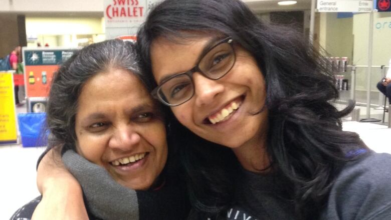 Two women grin and put with their arms around each other. 