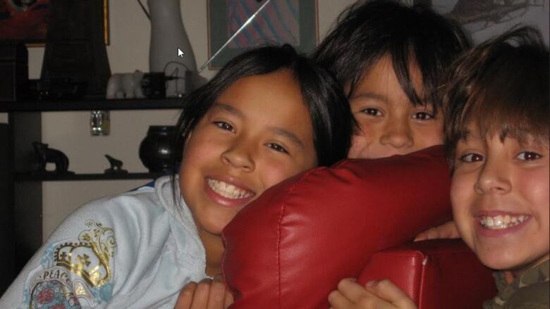 Three children with their heads pressed close together smile for the camera.