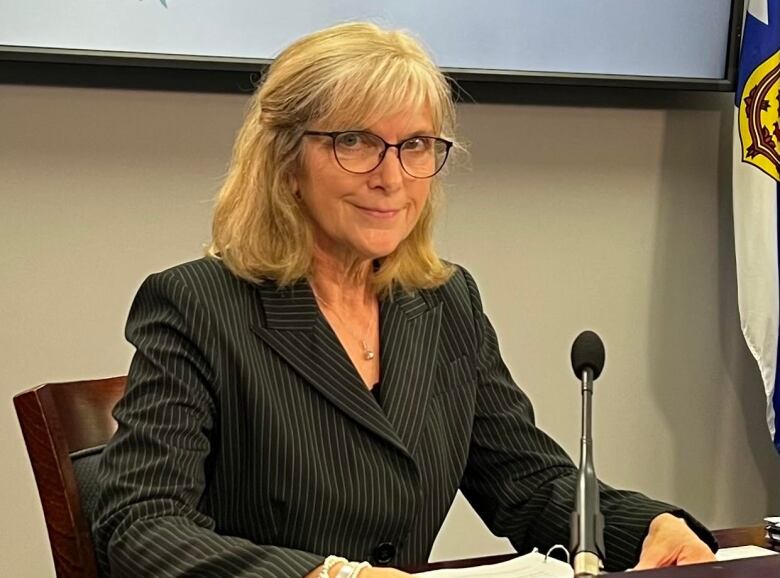 A woman wearing glasses and a pinstriped suit seated at a table.