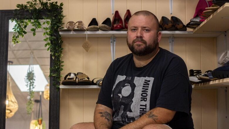 A seated man with shoes behind him, stares into the camera grimly.