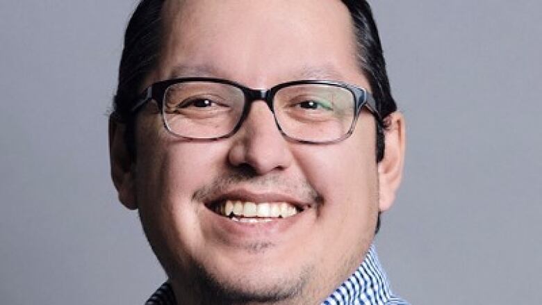 Close-up of a smiling individual wearing glasses and a blue and white checked shirt. 