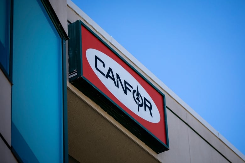 A red sign with a white oval that says Canfor.