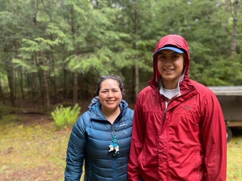 Mother and son in raincoats in green forest.