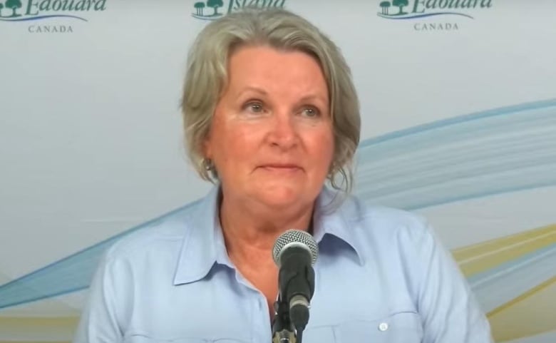 A woman in a blue shirt sits in front of a microphone. 