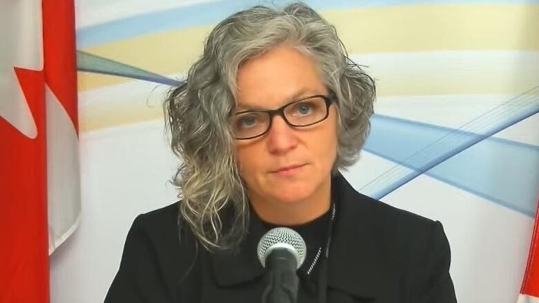 Woman in a black jacket sits in front of a microphone. 