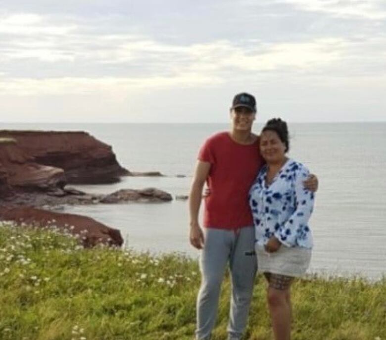 Tall young man, woman, on a grassy ledge near water.