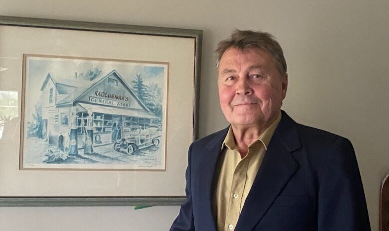 A man in a suit jacket smiles next to an old sketch drawing of a general store.