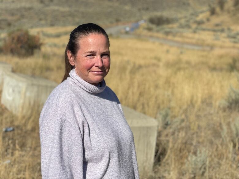 A woman smiles while standing among dry grass.