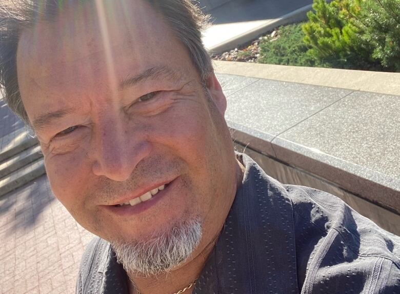 A man smiles in front of a city hall building.