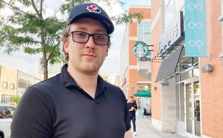 Portrait of man wearing a ball cap in front of stores in uptown Waterloo.