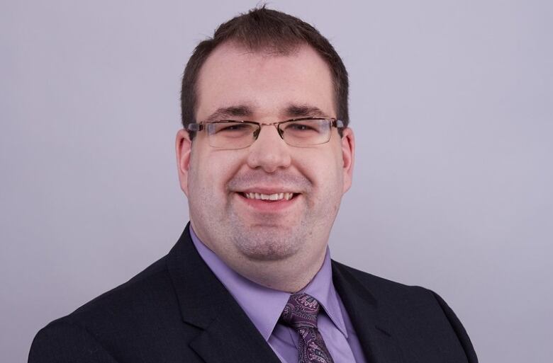 A man wearing a suit and glasses poses and smiles.