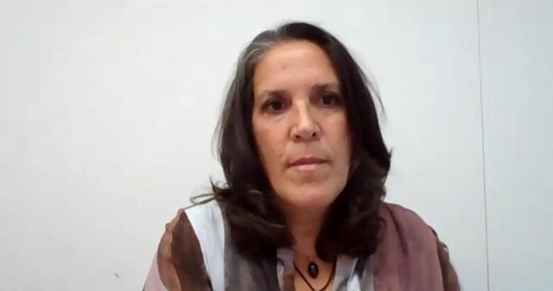 A woman sits in front of a white wall. 