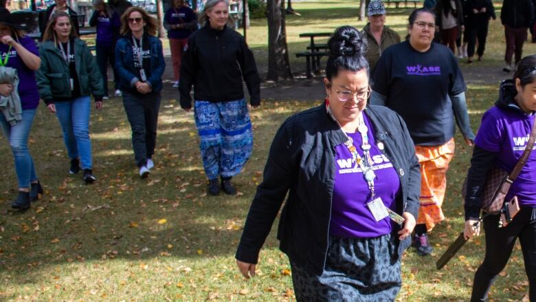 A group of people walk together wearing ribbon shirts and purple shirts.