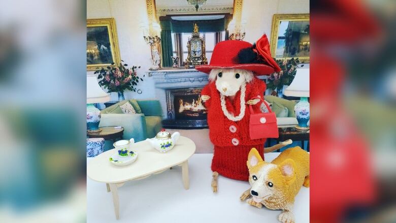 A taxidermied rat posed in front of a sitting room, with a teaset and a toy dog next to it.