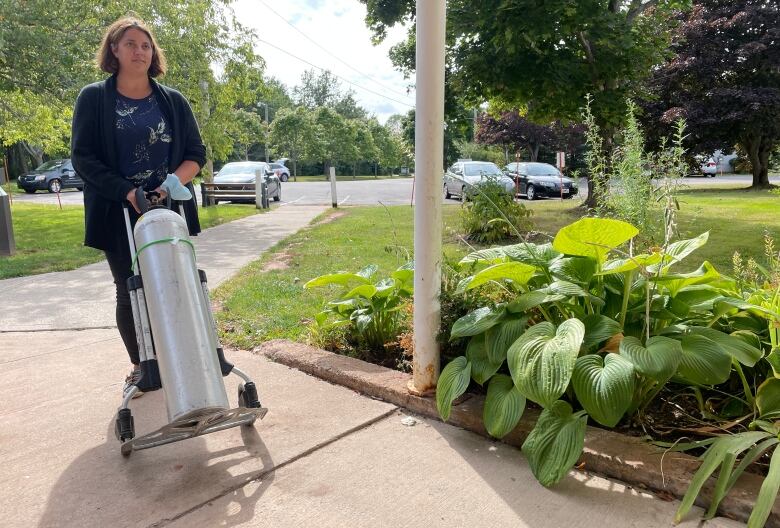 Woman wheels an oxygen tank down a sidewalk. 