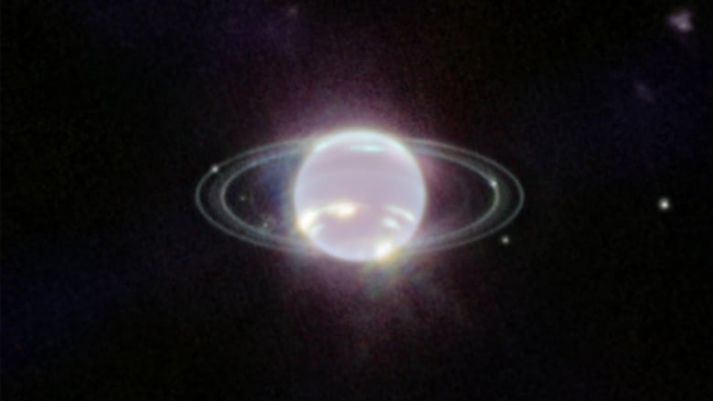 An almost pearlescent planet seen with two bright rings circling around it, with white dots representing the moons seen intermingling with the rings.