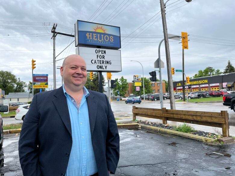 A bald man in a suit jacket smiles in front of a restaurant sign.