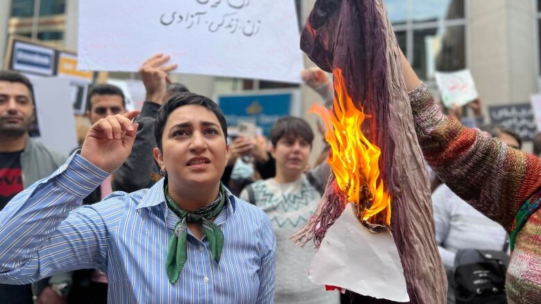 Protesters gather while a headscarf burns in the picture's foreground.