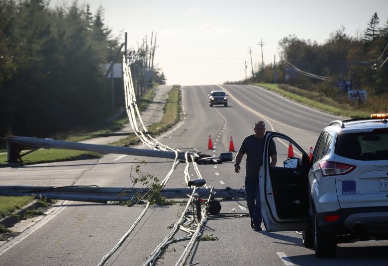 An Eastlink cable employee walks downed telecommunication lines at the entrance to J.A. Douglas McCurdy Sydney Airport. A truck is driving towards him. 