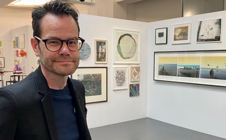 A man in a blazer stands in an art exhibit. 