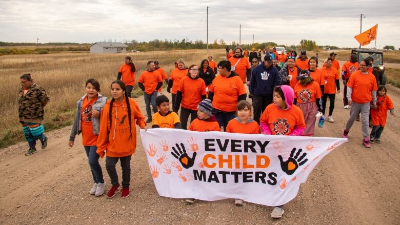 Dozens of people wearing orange shirts walk holding a sign that says 