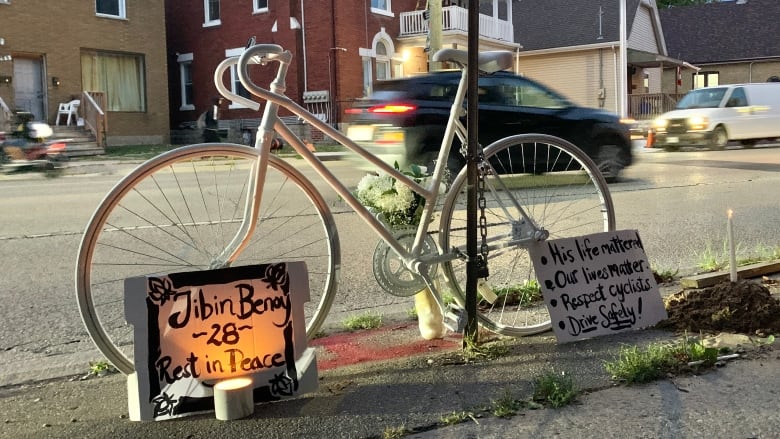 A white bike on the side of the road is surrounded by candles and signs saying 