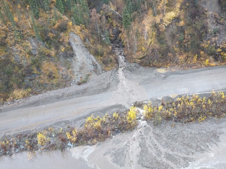 A section of highway is covered in debris with tracks of earth seen on the hill above the road.