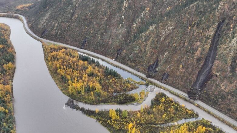 An aerial view of a section of a highway partially covered in debris, with tracks of earch coming from the side of the mountain beside it.