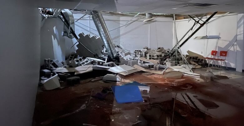 A room with ceiling tiles falling down and concrete building blocks from walls scattered around. 