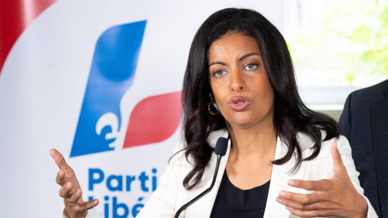 A woman wearing white gestures. In the background the Liberal L logo.