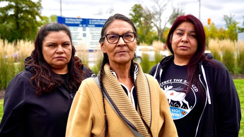 Three women look into the camera with serious faces.