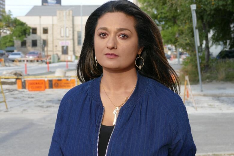 A woman with long hair wearing a blue jacket looks serious in front of a street under construction.