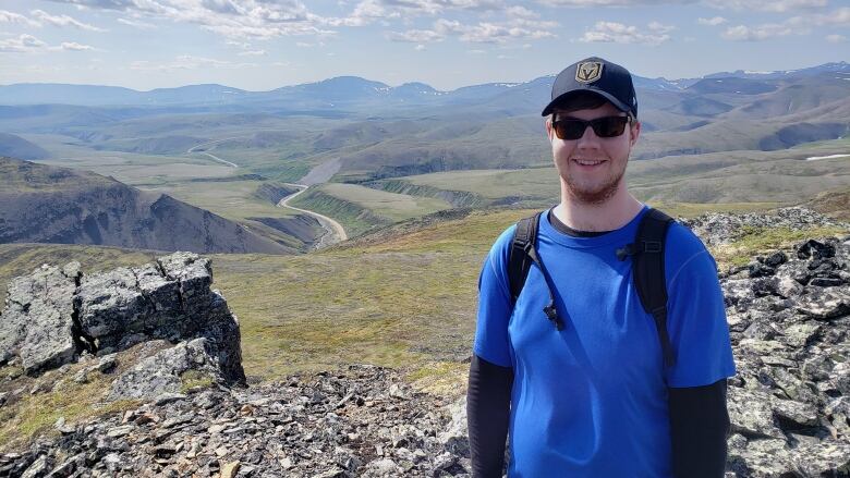 Smiling man standing in front of a winding highway and mountains as far as the eye can see.