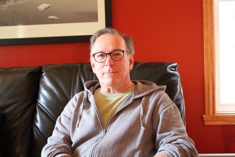 A man wearing a grey hoodie sits in a room with red walls. 