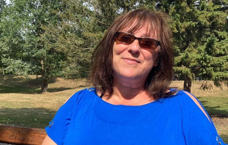 Portrait of woman in bright blue shirt with trees in background.