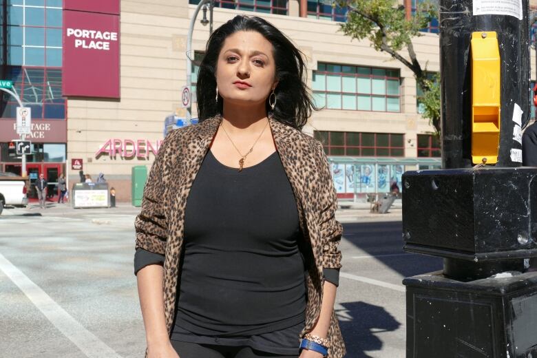 A woman wearing an animal print jacket and black shirt is standing in front of a large building with a sign reading 