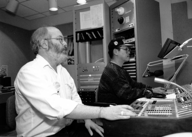 Two men sit in a studio with their hands on a switchboard.