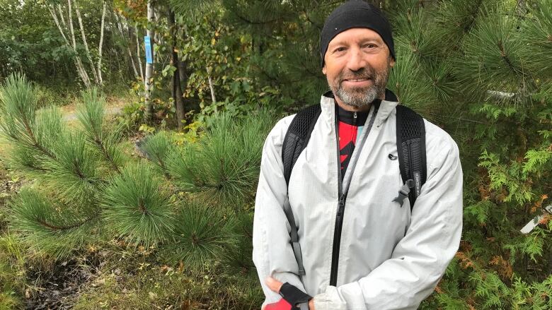 Chris Gore smiles as he stands in front of a pine tree on a cool autumn day in Sudbury.