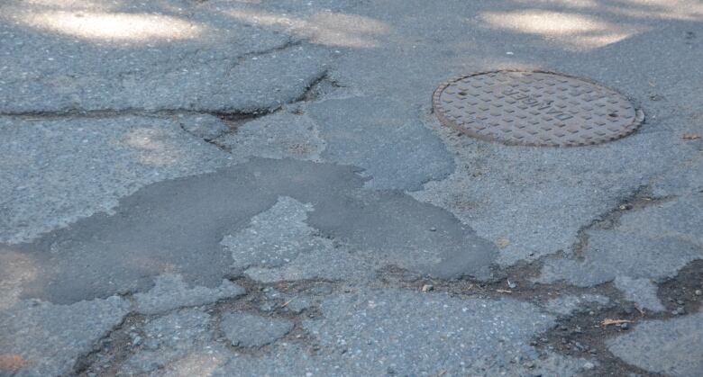 A street with lots of pavement patches in the area surrounding a manhole cover. 