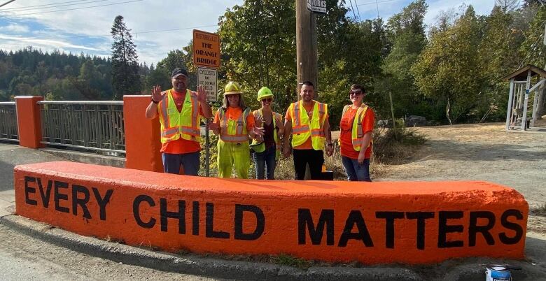 A group of people in high-vis vests stand over a barricade reading 'Every Child Matters'.