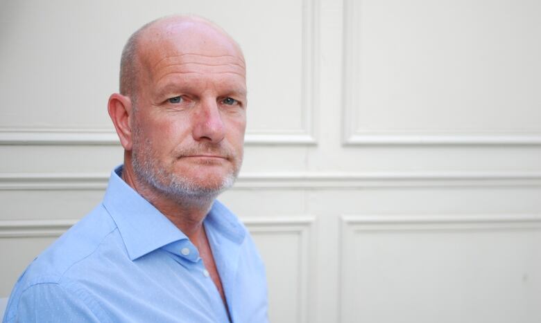 A man with a shaved head in a blue shirt poses for the camera.