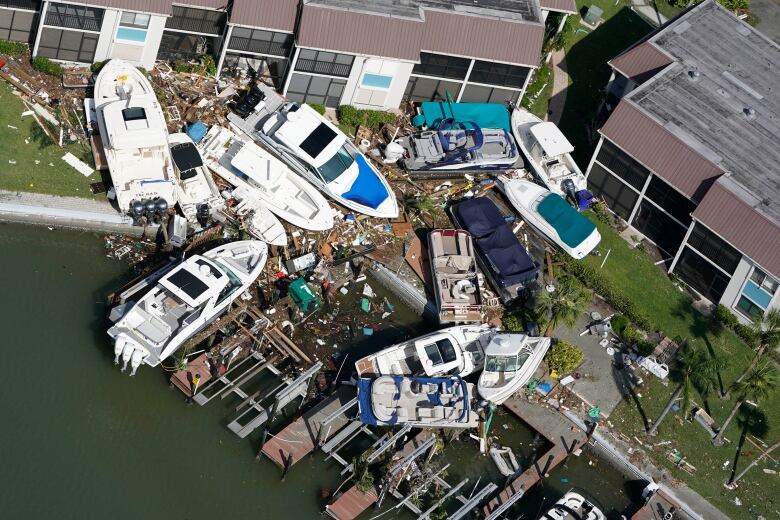 Overhead shot of damaged pleasure boats washed up on the shore, beside buildings, amid wreckage.