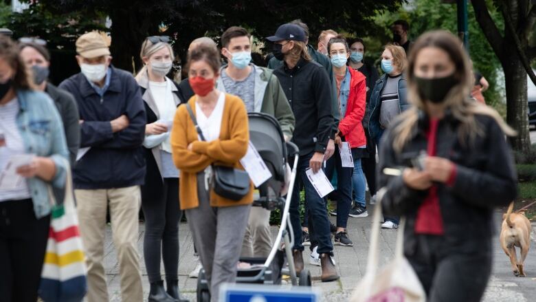 A group of masked voters are seen lined up outside a polling station.