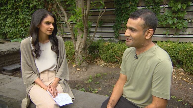 Anita Bathe and Hamid Habibi sit facing each other on a low stone wall during an interview.