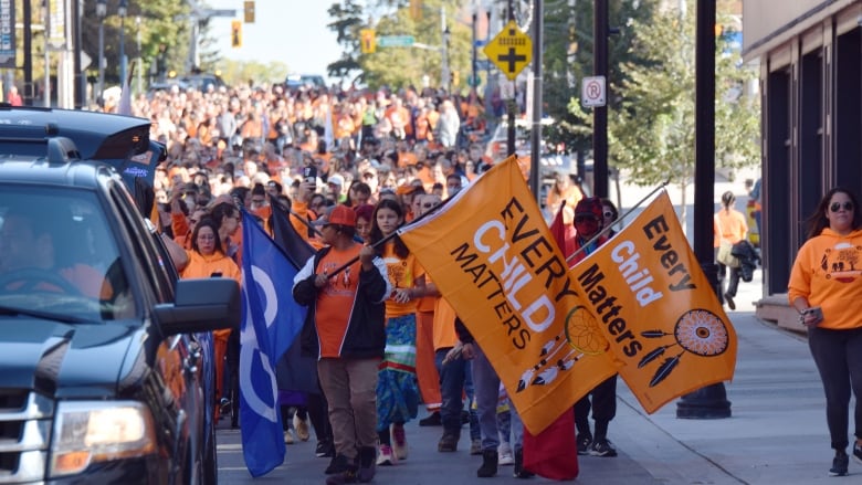 Group of people in orange shirts walk down city street as part of march.