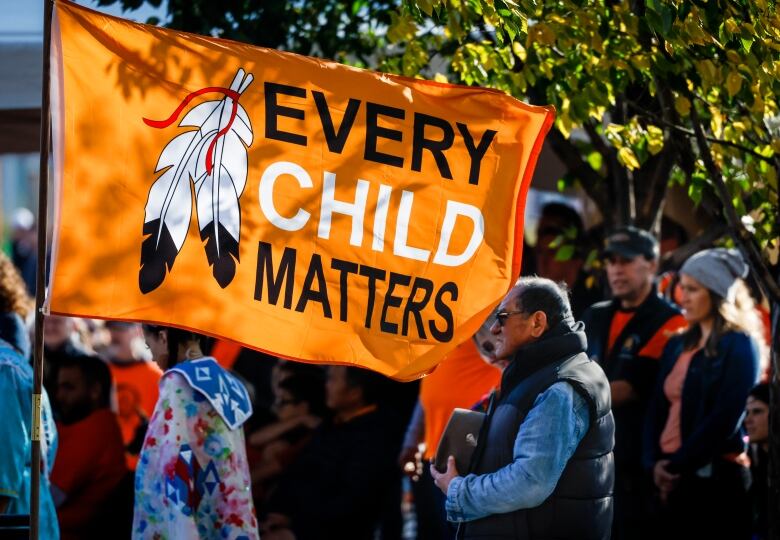 A crowd walks and carries an orange flag that says Every Child Matters 