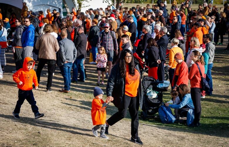 A crowd wearing orange walks on grass