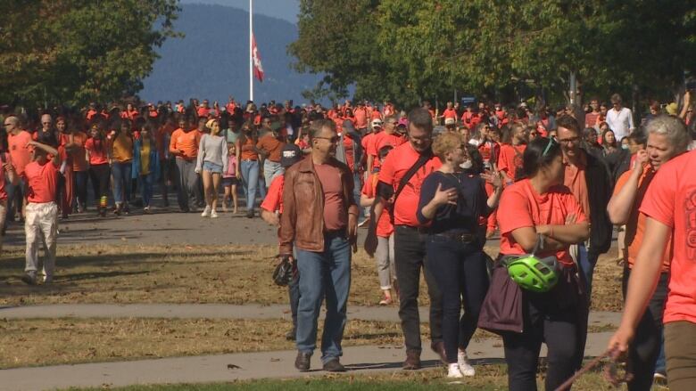 Dozens of people wearing orange garments walk along a boulevard.